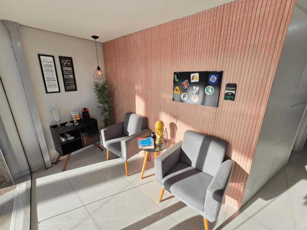 Coworking em Betim: muito além de um espaço para trabalhar 1 Sala de convivência da Elo Coworking em Betim com poltronas cinza. planta, armário, iluminação pendente e parede amadeirada.
